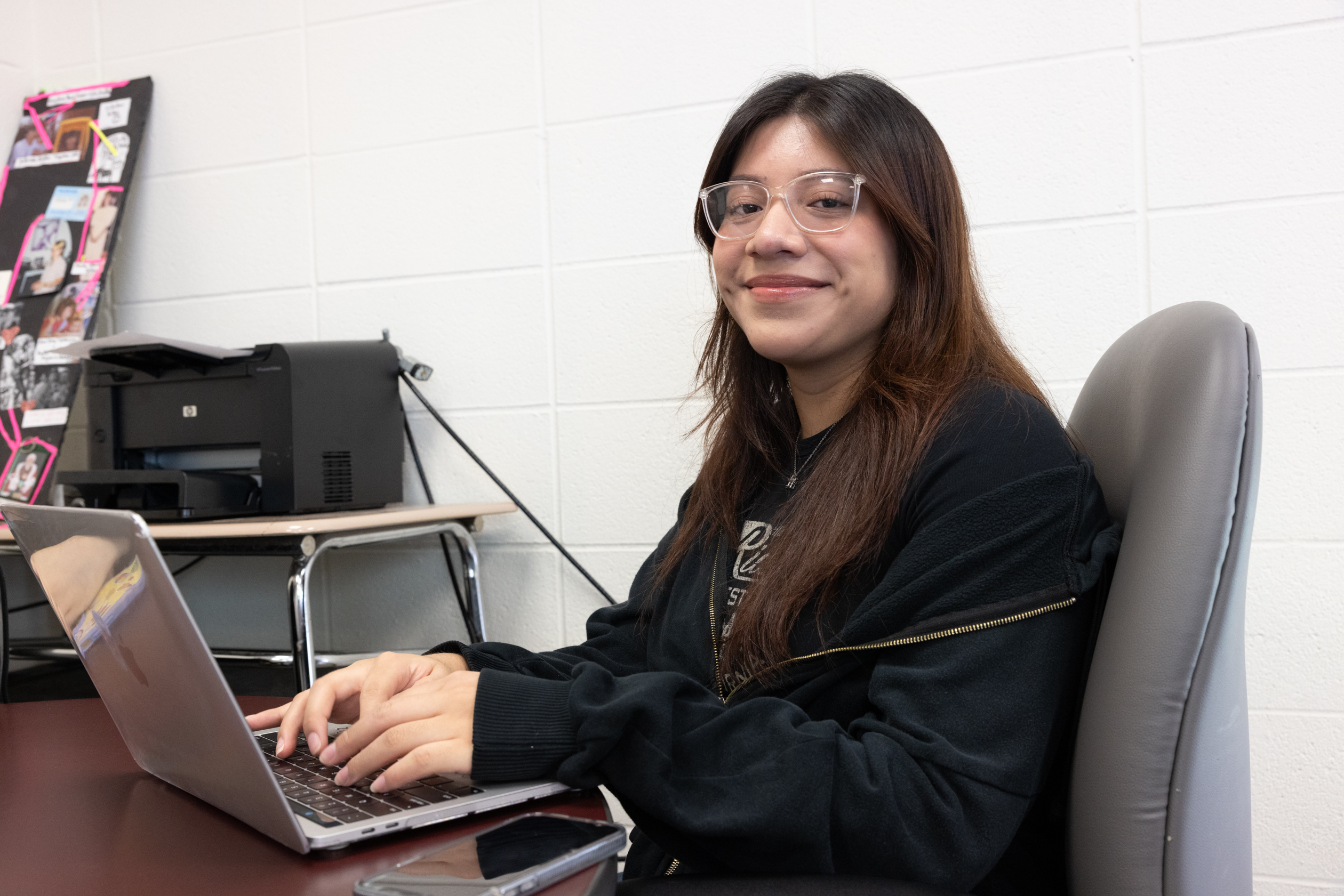 student smiling at camera working on laptop