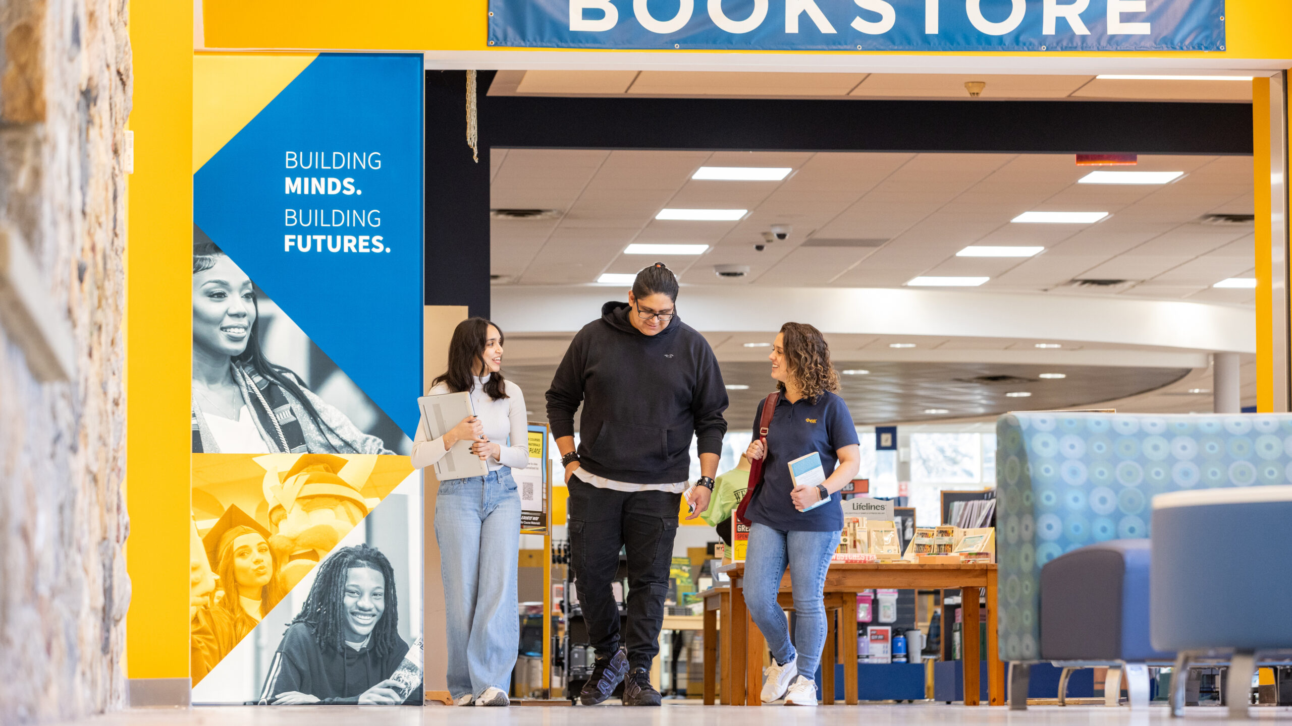 Three students talking while exiting the Bookstore. Banner with the slogan, 